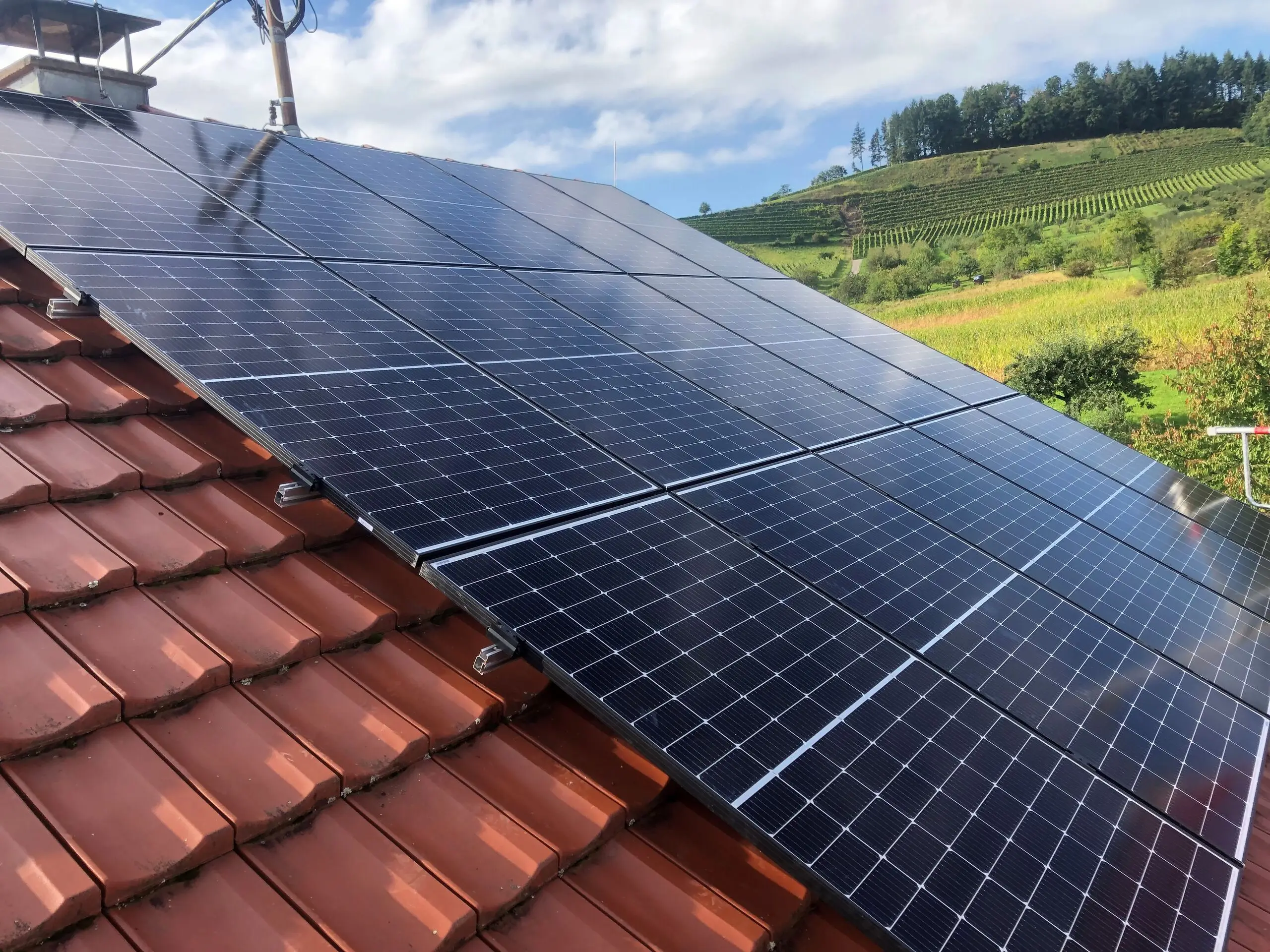 Photovoltaikmodule auf einem roten Ziegeldach, dahinter Weinberge in der Ortenau