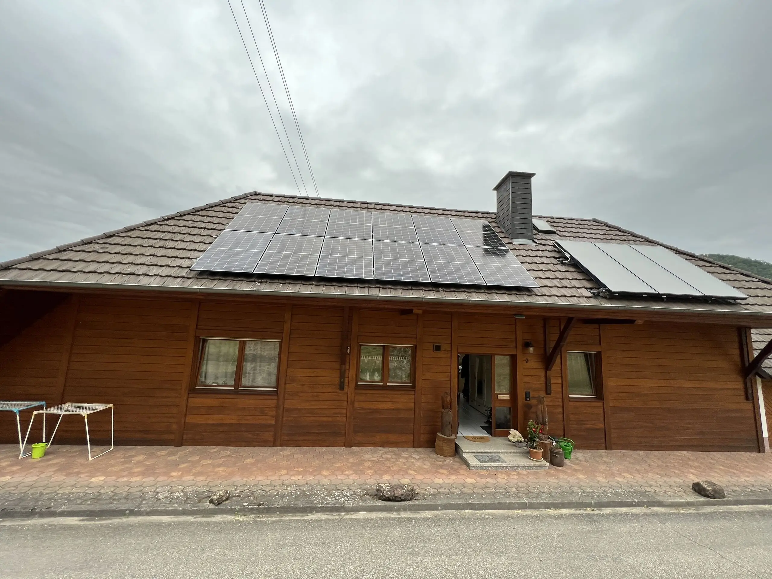 Wohnhaus mit dunkler Holzfassade, auf dem Ziegeldach Photovoltaikmodule und daneben Solarthermie-Kollektoren