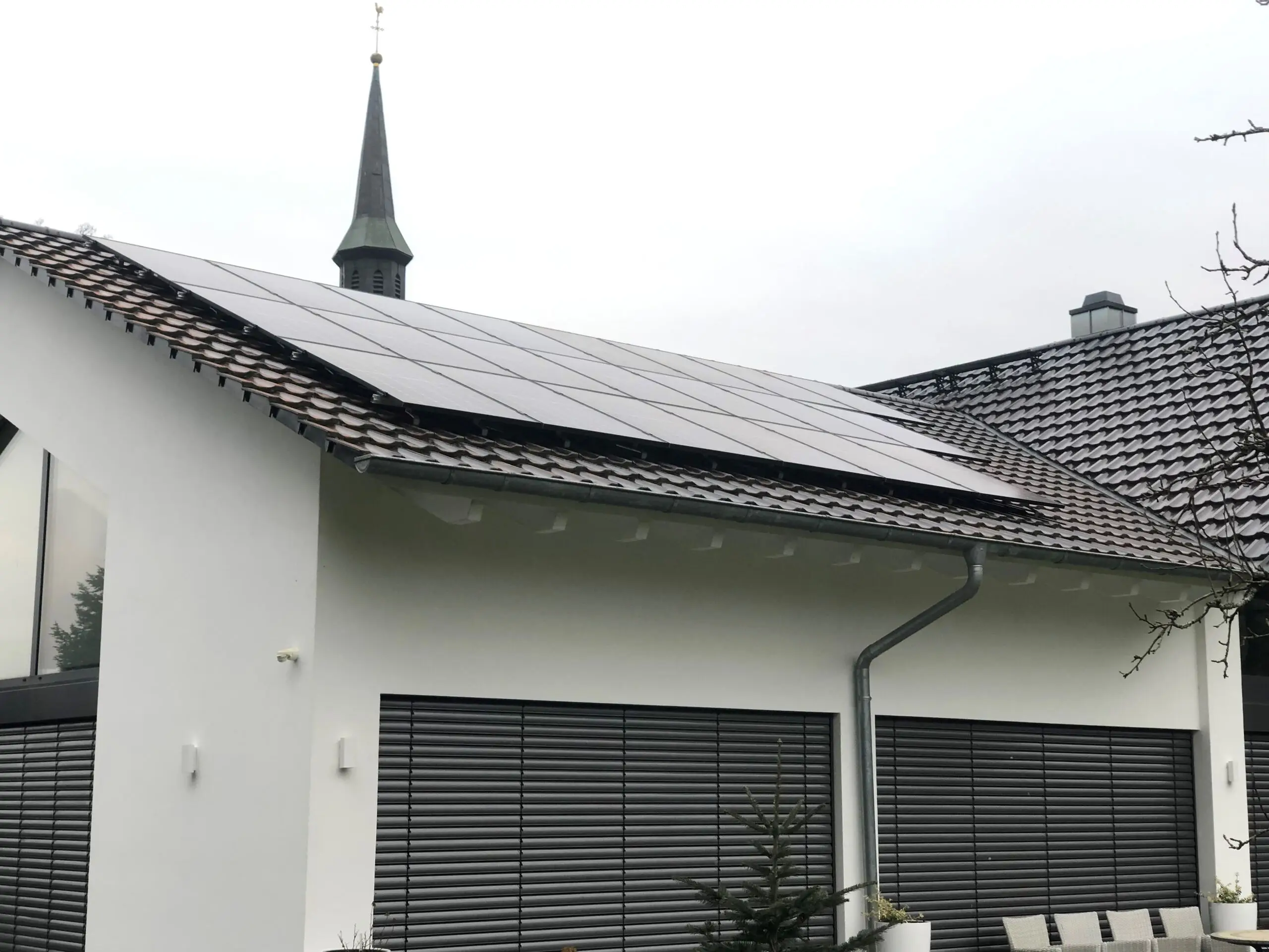 Wohnhaus mit vollschwarzer Photovoltaikanlage, dahinter ein Kirchturm