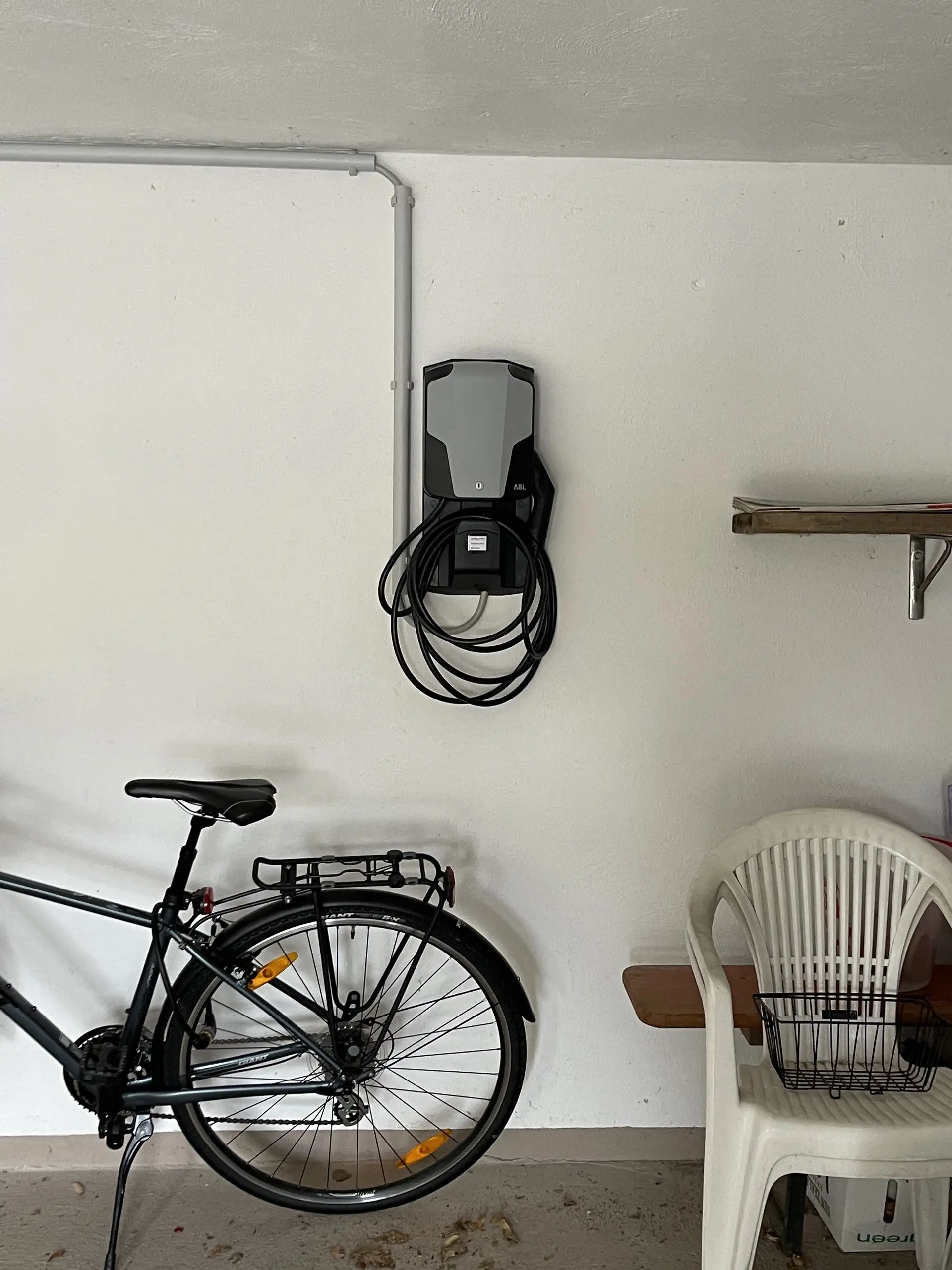 Wandmontierte Wallbox mit aufgewickeltem Ladekabel in einer Garage, daneben steht ein Fahrrad