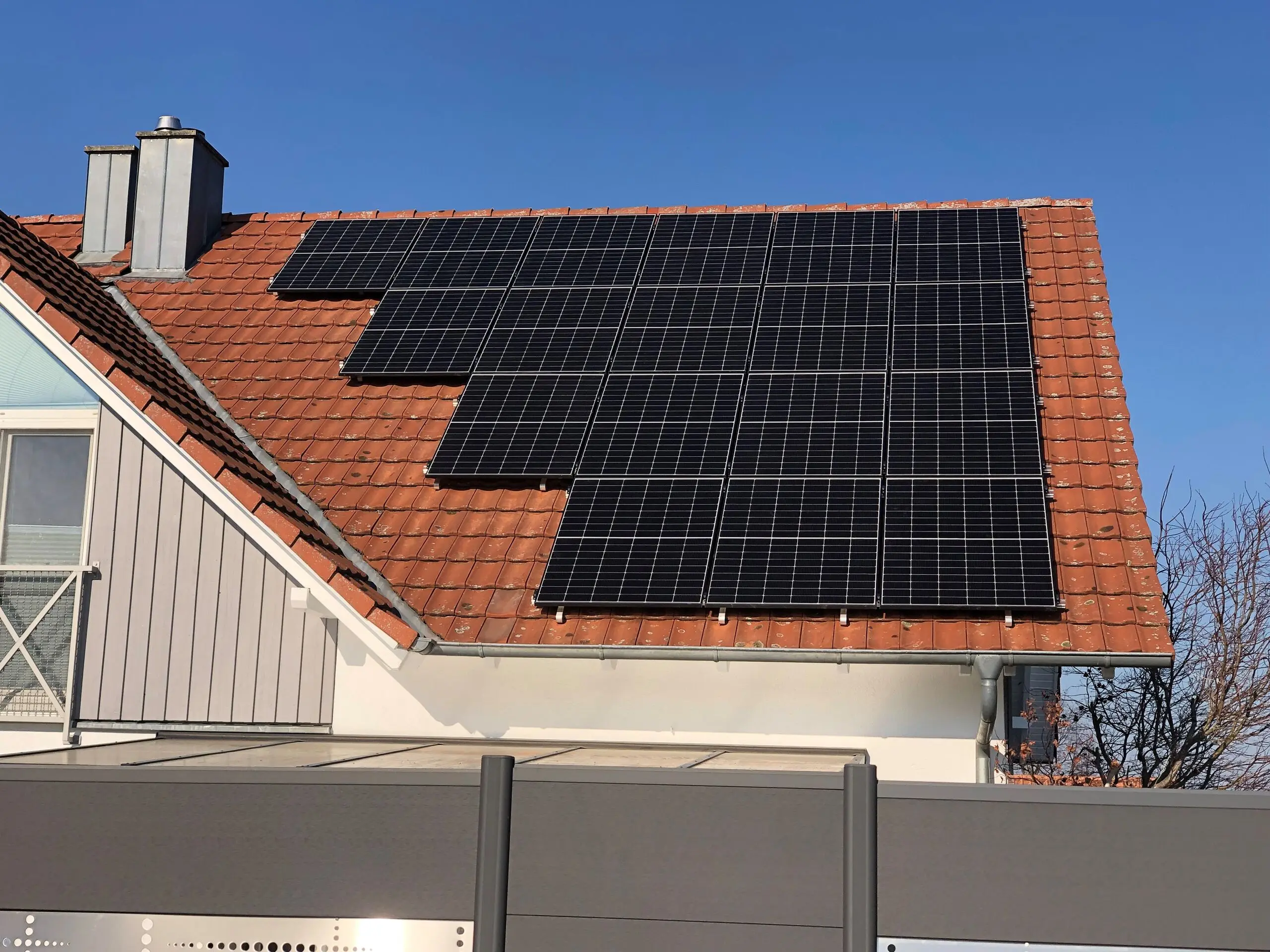 Photovoltaikmodule auf einem roten Ziegeldach vor blauem Himmel